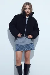 Campera puffer de corderito negro con cuello alto y diseño oversized. Presenta una textura tipo teddy, cierre frontal y corte a la cintura.