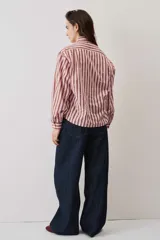Camisa a rayas verticales en tonos rosado y marrón, de manga larga abullonada, cuello camisero y cierre frontal de botones con pequeños apliques brillantes.