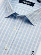 Camisa de vestir de hombre a cuadros celestes y blancos, de corte clásico, con cuello italiano y logo bordado en el frente.