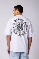 Remera oversize de corte holgado, color blanco, con cuello redondo y mangas cortas. Presenta un pequeño estampado circular en el centro del pecho con un diseño abstracto inspirado en arrecifes.