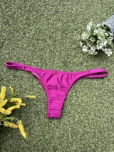 Bikini de tela metalizada color magenta, compuesto por un top con breteles finos y detalle de hebilla metálica en el centro, y una bombacha tipo colaless.