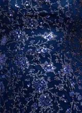 Vestido corto de un solo hombro, confeccionado en tul azul marino con forro interior. Presenta un diseño ajustado al cuerpo, decorado con lentejuelas y brillos distribuidos en un patrón floral sutil, con un borde de cuentas oscuras en el escote.