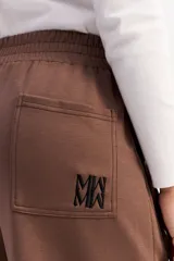 Pantalón de corte ancho y relajado en color marrón, con cintura elástica, bolsillos laterales y costuras verticales decorativas en contraste a lo largo de las piernas.