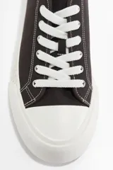 Zapatillas deportivas bajas de lona color marrón oscuro, con cordones blancos y suela de goma blanca con diseño acanalado.