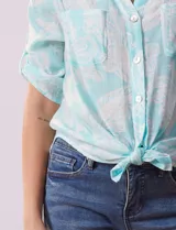 Blusa celeste con estampado blanco, de gasa, con cuello a la base y escote en V. Tiene abertura con botones, bolsillos delanteros y mangas 3/4 regulables con presilla y botón. El ruedo termina con un nudo.