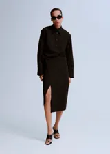 Falda midi cruzada color negro, de tiro alto y con tajo frontal.