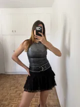 Cinturón ancho de cuero negro con hebilla metálica circular y doble hilera de tachas plateadas.