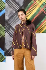 Camisa de gabardina marrón con estampa a cuadros y rayas diagonales, diseño plisado en el frente y detalle de aplique floral de plumas en el cuello.