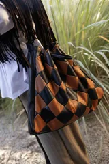 Bolso de hombro tipo hobo con diseño de rombos entrelazados en cuero negro y marrón. Presenta una silueta amplia y flexible con detalles de flecos largos en la parte superior.