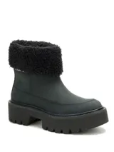 Bota de caña media color negro, confeccionada en nubuck con cuello de piel sintética negra. Presenta una suela de plataforma dentada de goma y diseño robusto.