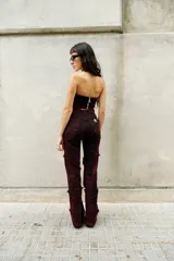 Pantalón de denim elastizado con efecto de lavado desgastado en tono bordó oscuro. Presenta un diseño de corte entallado con recortes irregulares, costuras expuestas con terminaciones desflecadas y tiro alto.