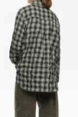 Camisa de corte recto y largo medio, confeccionada en tejido de algodón con textura. Presenta un diseño de cuadros en tonos rojo, negro y azul, cuello camisero, cierre frontal con botones, manga larga con puños abotonados y bolsillo de plastrón en el pecho.