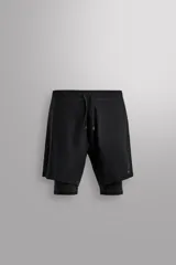 Pantalones cortos de entrenamiento 2 en 1 de Zara Athleticz, confeccionados en tejido técnico ligero con malla interior ajustada. Presentan cintura elástica con cordón de ajuste, bolsillos laterales con cierre de cremallera y aberturas en el bajo.