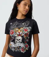 Remera de algodón con escote redondo y mangas cortas, de corte ajustado al cuerpo y color negro. Presenta un estampado frontal de estilo tattoo flash con un tigre, una calavera, panteras y rosas, acompañado de la inscripción "Liberty" y detalles de brillos termosellados.