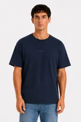 Remera de manga corta color azul marino, con cuello redondo y diseño holgado. Presenta un pequeño texto sutil estampado en el centro del pecho.