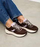 Championes estilo runner de la marca Satinato, confeccionadas en una combinación de poliuretano y mesh respirable. Presentan un diseño con recortes superpuestos en tonos marrón y detalles en lila, cierre con cordones bicolor, lengüeta acolchada, tirador trasero y una suela robusta con entresuela alta y base tractorada.