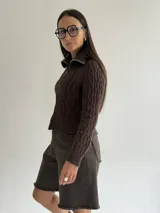 Sweater tipo campera de tejido de punto con diseño de trenzas, color blanco, con cuello alto y cierre frontal completo.