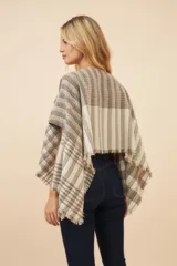 Poncho color beige con diseño a cuadros, cuello bote y terminaciones desflecadas. Tiene aberturas para los brazos en los laterales y detalles en cuero.