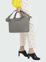 Bolso tipo tote de cuero gris, con diseño minimalista, doble asa de mano y correa de hombro ajustable y extraíble. Cuenta con cierre de solapa con botón a presión y cierre principal.