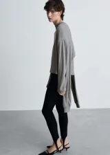 Buzo de punto fino color gris melange, con cuello redondo y diseño de mangas con solapas decorativas superpuestas. Presenta un corte recto y mangas largas con puños ajustados.