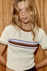 Top de tejido rústico con cuello redondo y manga corta. Presenta un diseño de base color crema con detalles de rayas horizontales en tonos marrón y lila en el pecho y los puños.