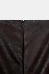 Vestido corto de Zara con efecto piel, cuello barco y diseño sin mangas. Presenta un bajo abullonado con elástico interior y cierre de cremallera en la espalda.