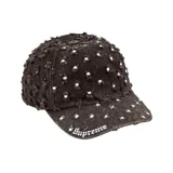 Gorra de denim negro con detalles desgastados y aplicaciones de pedrería dispersas por toda la superficie, con visera curva y el logotipo bordado en la parte frontal.