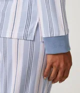 Pijama largo de dos piezas con estampado de rayas verticales en tonos azul, blanco y rosa. La blusa es de manga larga con cuello redondo y puños ajustados en ribana azul. El pantalón es largo, con cintura elástica y puños ajustados en ribana azul.