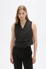 Chaleco negro sin mangas con escote en V y cierre frontal con botones. Diseño corto con solapas simuladas a la altura de la cintura.