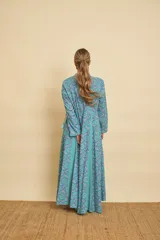 Vestido largo de algodón con estampado de mandalas en tonos celestes y azules, combinado con gajos laterales lisos en color turquesa. Presenta cuello mao con escote en V, mangas largas y silueta amplia y fluida.