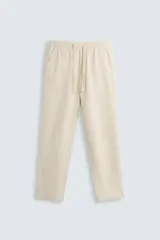 Pantalón de corte relajado color beige confeccionado en tejido de mezcla de algodón y lino. Posee cintura elástica ajustable con cordón, bolsillos frontales y bolsillos traseros de vivo.