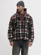 Sobrecamisa de textura tipo teddy con estampado de cuadros en tonos marrón, negro y crema. Presenta cuello camisero, cierre frontal de botones, bolsillos en el pecho y puños abotonados, con un corte relajado.
