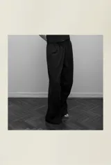 Pantalón negro de algodón con pretina elástica, bolsillos laterales y pinzas horizontales en las rodillas.