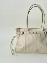 Bolso grande de cuero marrón con textura tipo cocodrilo, estructura rígida y asas para llevar al hombro. Tiene una tira con tachas y hebillas en cada extremo, también lleva lazos en los costados.