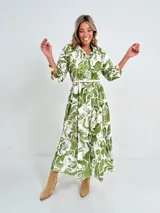 Vestido camisero midi de algodón con estampado floral en tonos rosados y blancos. Tiene cuello camisero, mangas 3/4, botones frontales, falda escalonada y cinturón fino.