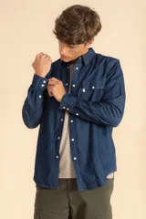 Camisa de jean azul de manga larga, con cierre frontal de botones a presión, dos bolsillos frontales con solapa y costuras reforzadas.