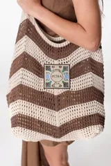 Bolso tejido a crochet con diseño a rayas horizontales en tonos marrón y beige. Tiene un parche cuadrado con el texto "Flowers Petra Club" y asas de hombro.