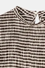 Top de cuello redondo con diseño de nido de abeja elástico en el cuerpo. Presenta mangas abullonadas con puños elásticos y un detalle de volado en el ruedo. Cuenta con cierre de botón en la espalda.