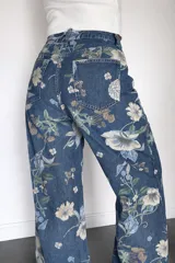 Pantalón de jean corte wide leg con estampado floral en tonos azules, verdes y blancos. Presenta tiro alto, diseño de pierna amplia y bolsillos traseros.