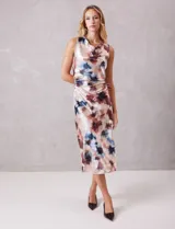 Vestido midi de satén fluido con estampado floral en tonos beige, azul y borravino. Presenta cuello volcado, diseño sin mangas y un drapeado lateral fruncido en la cintura que aporta movimiento a la falda de corte evasé.