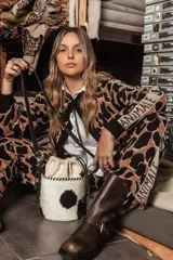 Cartera tipo canasta de cuero con estampado animal print de vaca en blanco y negro. Tiene correa larga de cuero negra y herrajes metálicos plateados.