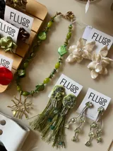 Caravanas colgantes artesanales con base verde y flecos largos de hilo en tono verde oliva, adornadas con pedrería y abalorios brillantes.