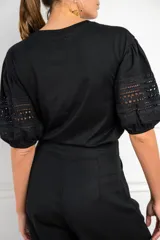 Remera negra de algodón con mangas cortas abullonadas que presentan detalles de encaje bordado y calado en los extremos.