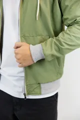 Campera verde oliva de nylon anti-lluvia, con capucha, cierre frontal y puños y cintura en tejido de punto gris. Presenta un logo bordado en el pecho.