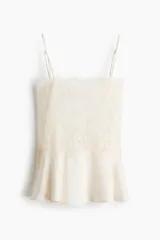 Top de encaje color crudo con escote recto y breteles finos ajustables. Modelo entallado con peplum levemente acampanado en tejido con brillo sutil.