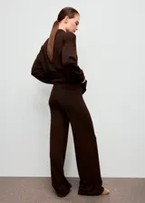 Pantalón de punto color marrón oscuro, de tiro medio, cintura con goma elástica y diseño recto y largo. Cuenta con detalle de costuras verticales.