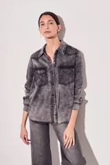 Camisa de denim gris con efecto lavado, corte recto, cuello clásico, cierre frontal con botones a presión, dos bolsillos con solapa en el pecho y mangas largas con puños abotonados.