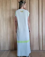 Vestido largo de tejido de punto en color crudo, con detalles en color amarillo neón en las mangas y en la parte inferior. Presenta cuello redondo, mangas cortas y tajos laterales en el ruedo.