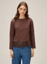Remera de manga larga en color marrón, confeccionada en una combinación de tejido de punto y tela plana. Presenta un diseño de superposición frontal con costura decorativa en contraste y un panel inferior de textura diferenciada.