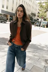 Blazer de corte estructurado en color marrón chocolate, con cuello solapa, hombros marcados y cierre frontal cruzado con botón oculto. Presenta un bolsillo superior tipo ojal y un diseño de bajo redondeado.